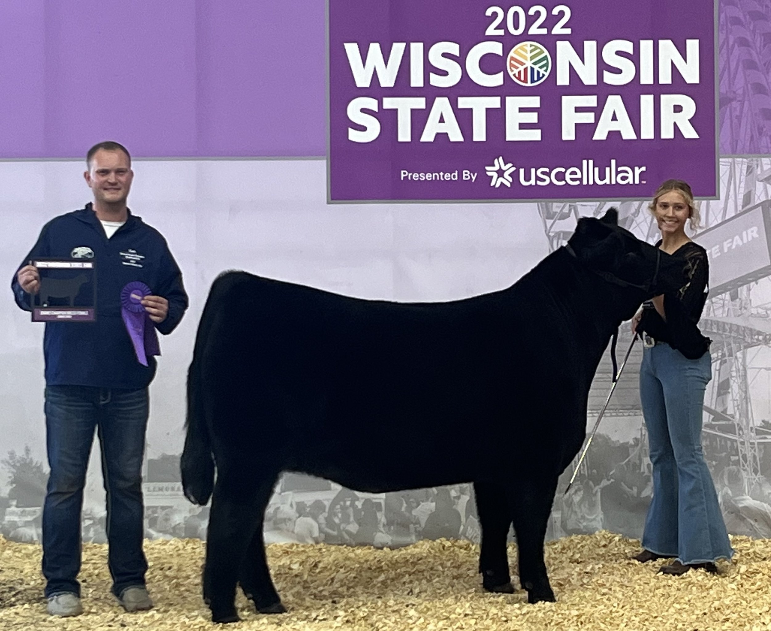 2022+Casha+Bacdrop+WI+State+Fair+ Young woman smiling while holding a chicken in a barn, showcasing a connection to farm life and animal care.